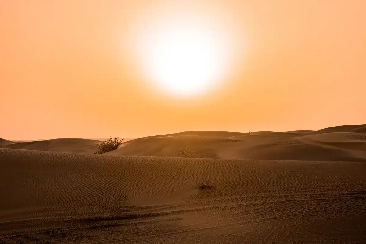 Termómetro mostrando temperatura extrema bajo sol intenso con paisaje seco y brumoso de fondo