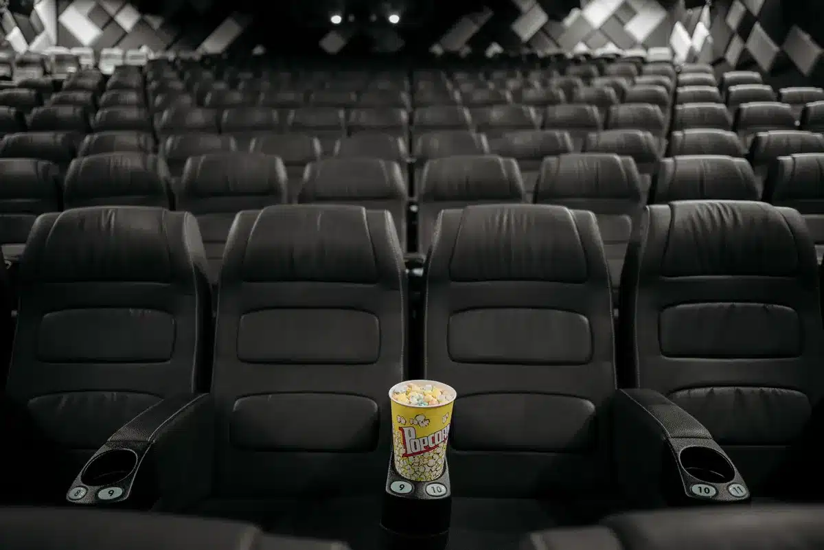 Vestíbulo de cine con carteles iluminados y múltiples pantallas de películas