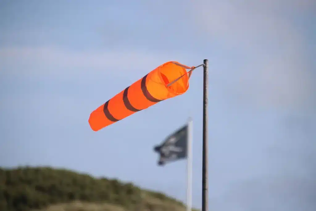 Personas resguardándose del viento intenso y calor extremo bajo un toldo, con objetos volando alrededor