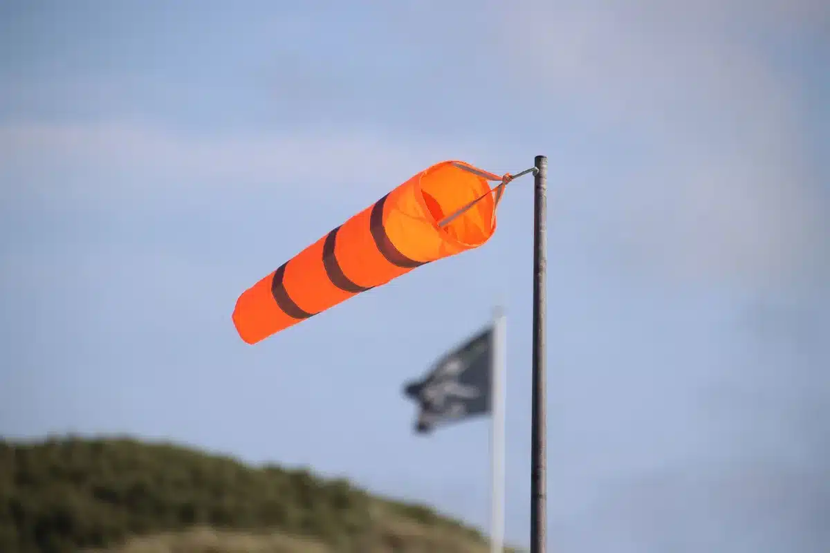 Personas resguardándose del viento intenso y calor extremo bajo un toldo, con objetos volando alrededor