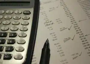 Manos anónimas sobre papeles y calculadora en escritorio, simbolizando trámites de pensión