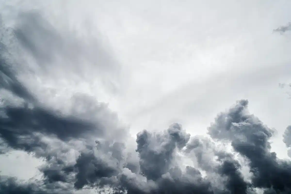 Persona de espaldas observando nubes oscuras y lluvia sobre una costa atlántica con montañas de fondo