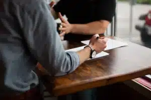 Manos anónimas pasando documentos sobre una mesa de reunión