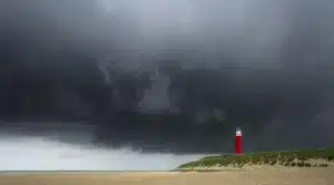 Playa rocosa con carbón esparcido y figuras anónimas de espaldas bajo cielo gris